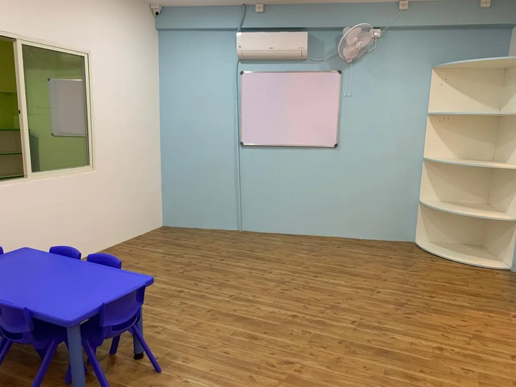 An empty preschool room with a low blue table, blue chairs, and a whiteboard