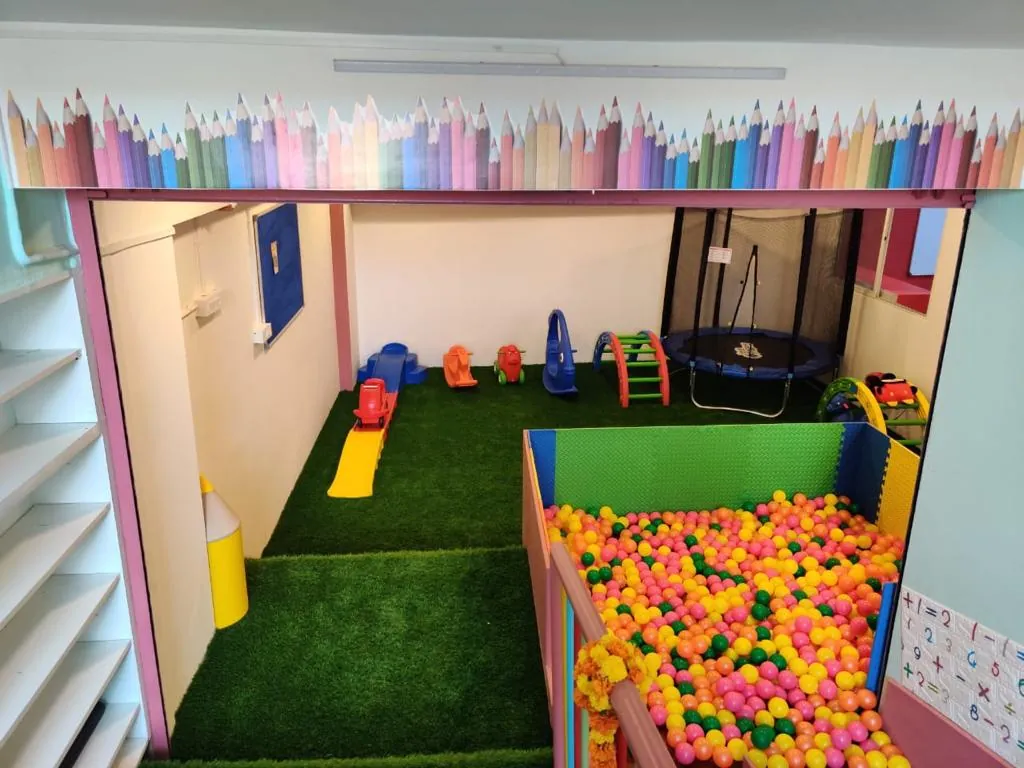 An indoor play area with green artificial turf, a ball pit of colourful balls, and a small slide